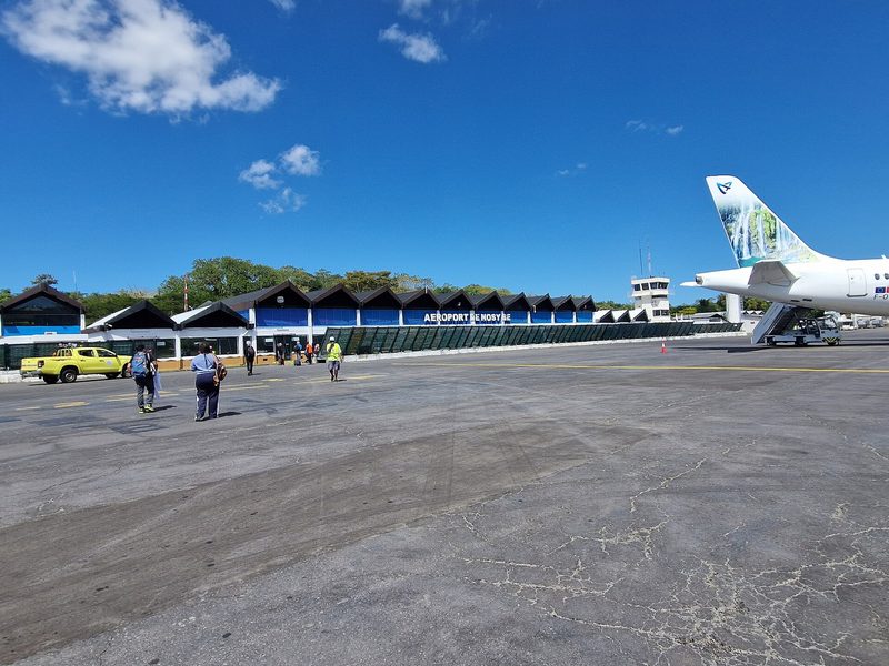 A turboprop aircraft on the apron at Fascene Airport, Nosy Be, with the blue AEROPORT DE NOSY BE terminal in the background